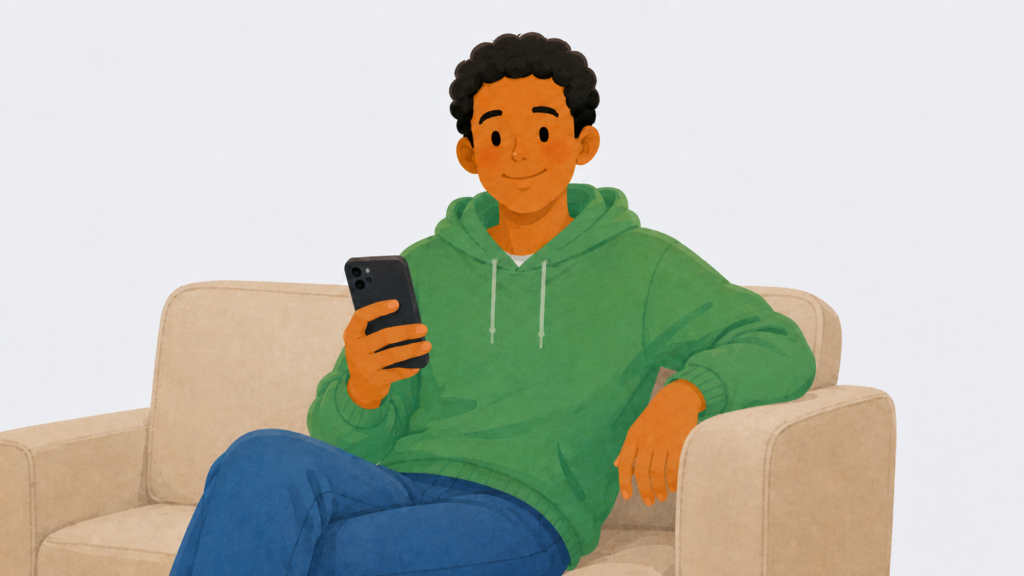 A young man in a green hoodie using a smartphone while sitting on a sofa